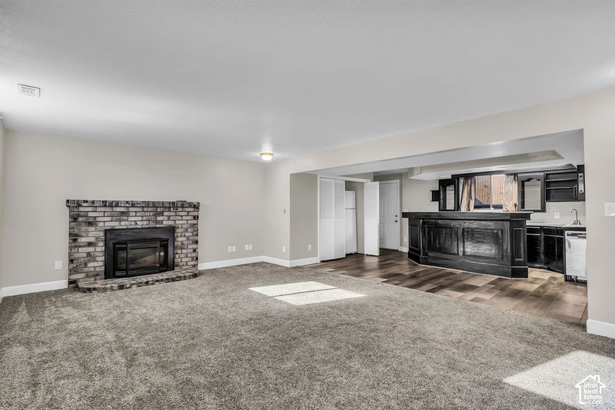 Gray brick fireplace with hearth, plush gray carpeting, wood-finish flooring, built-in wet bar, and recessed lighting