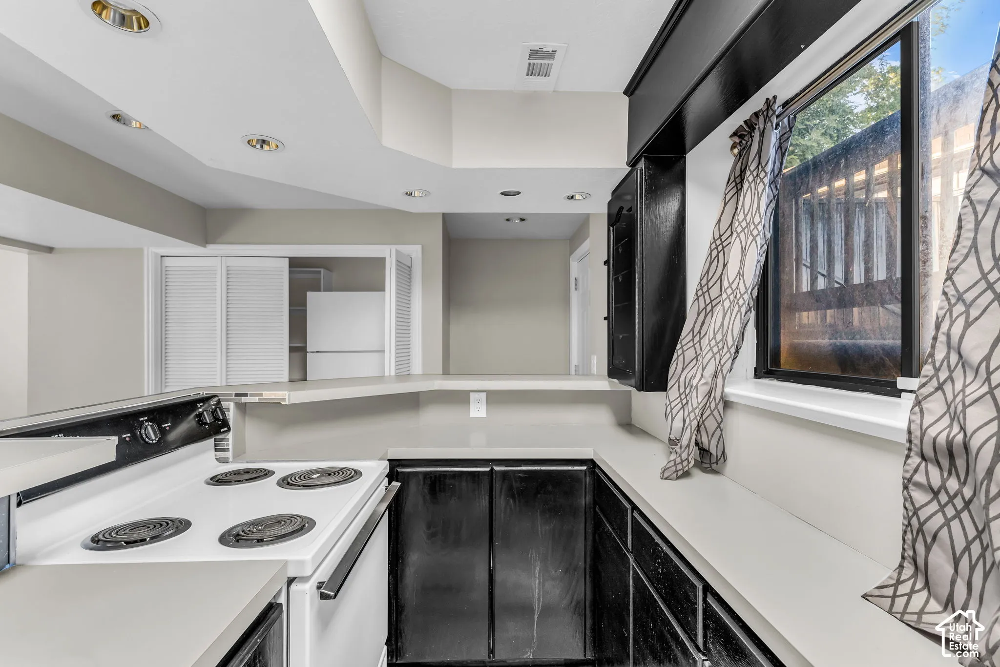 Kitchen area featuring a white electric range, dark cabinetry with light countertops, and recessed lighting