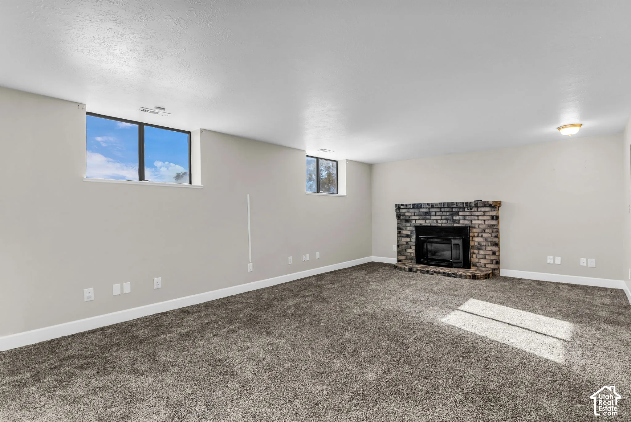 Neutral tone wall paint, grey carpeted flooring, and a corner brick fireplace with black insert