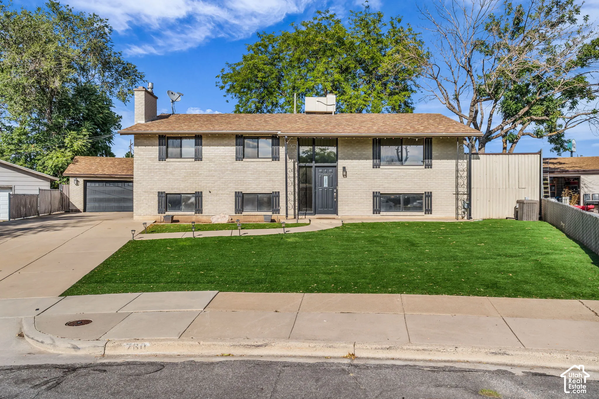 Brick exterior with dark shutters, front entry with sidelights, attached garage, concrete driveway, and a fenced yard