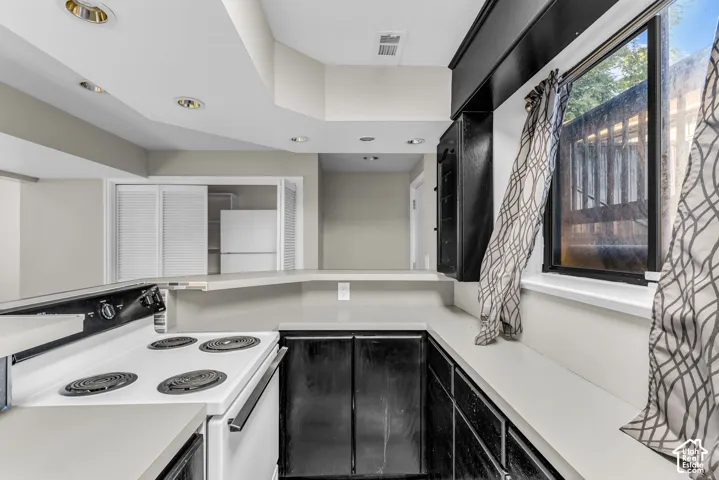 Kitchen area featuring a white electric range, dark cabinetry with light countertops, and recessed lighting