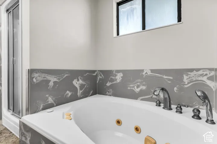 Built-in soaking tub with deck-mounted fixtures, separate shower enclosure with clear glass panel, and gray patterned tile wainscoting