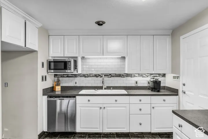 White cabinetry with crown molding, dark countertops, white subway tile backsplash, stainless steel appliances, and dark tile flooring
