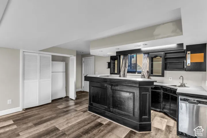 Wood-finish flooring, built-in bar with dark cabinetry, white countertops, and stainless steel dishwasher