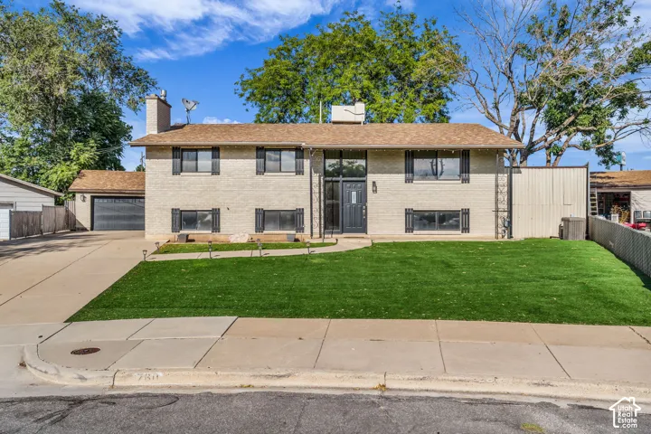 Brick exterior with dark shutters, front entry with sidelights, attached garage, concrete driveway, and a fenced yard