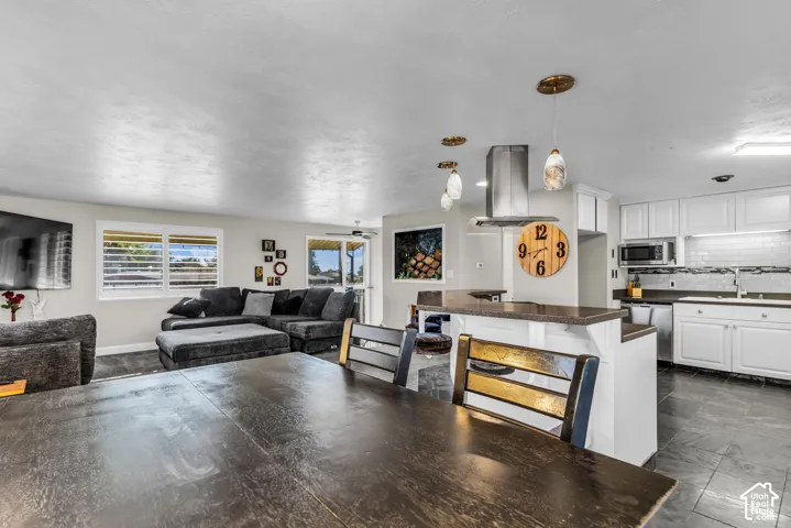Kitchen featuring white cabinetry, dark countertops, tiled backsplash, stainless steel appliances, and pendant lighting