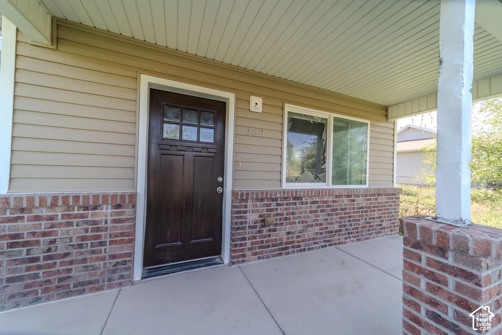 Covered porch with concrete flooring, brick wainscoting, and beige siding