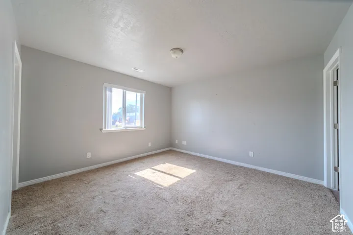 Textured carpet flooring, neutral painted walls, ceiling-mounted light fixture, and a window with white trim