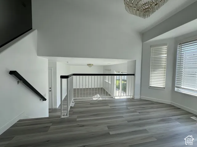 Spacious interior featuring wood-finish flooring, a tiered chandelier, a white spindle railing with a dark top rail, and multiple large windows with blinds