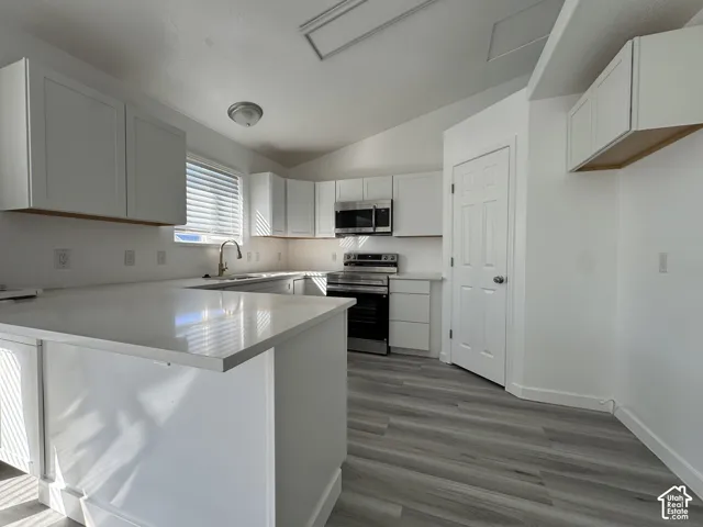 Modern kitchen featuring white cabinetry, light-toned countertops, stainless steel appliances, and wood-finish flooring