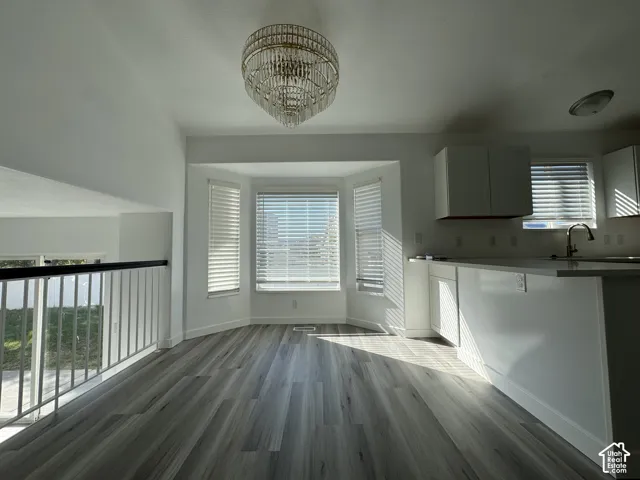 Wood-finish flooring, bay window, upper and lower cabinetry, kitchen sink with faucet, and a decorative chandelier