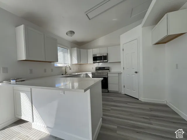 Kitchen featuring white shaker cabinetry, light-toned countertops, stainless steel appliances, and wood-finish flooring