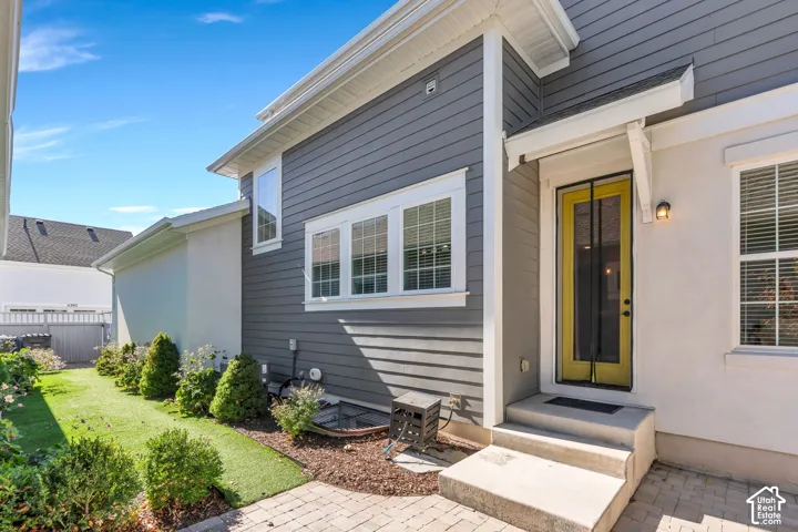 Two-tone exterior siding, covered entry, yellow paneled door, exterior wall sconce, paver patio, and landscaped yard