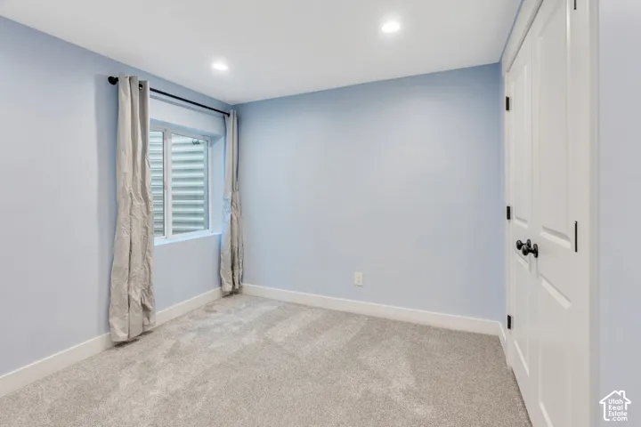 Recessed lighting, light blue wall paint, window with white trim, gray carpet, and white paneled doors with dark hardware