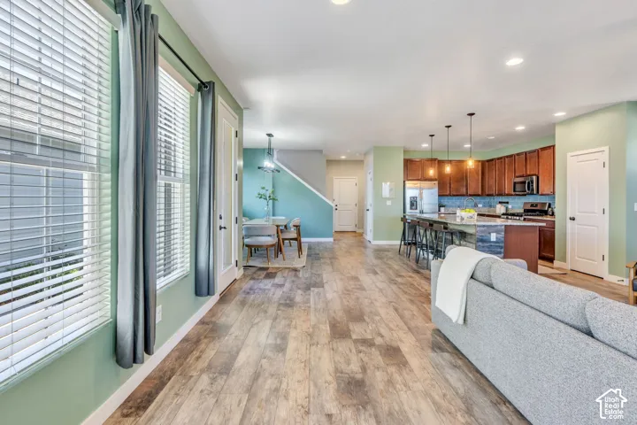Wood-finish flooring throughout the main living area, a kitchen featuring an island with pendant lighting, rich wood cabinetry, and a subway tile backsplash