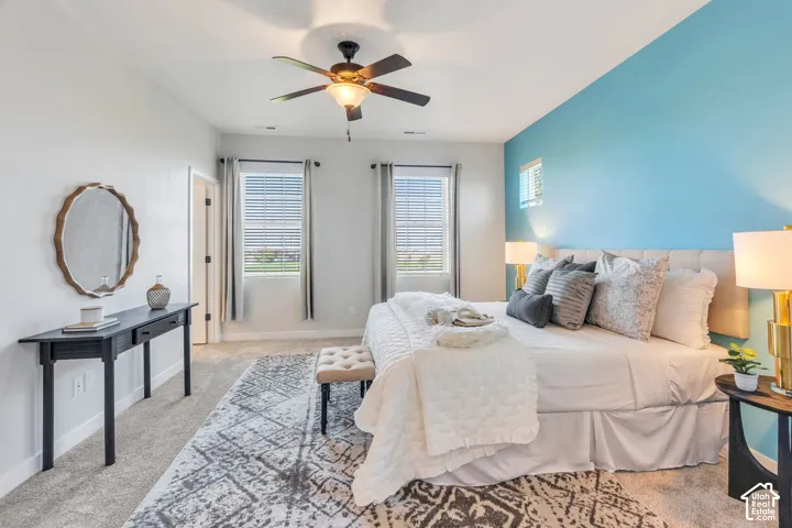 Carpeted flooring, two windows with blinds, built-in ceiling fan with light fixture, and a light blue accent wall