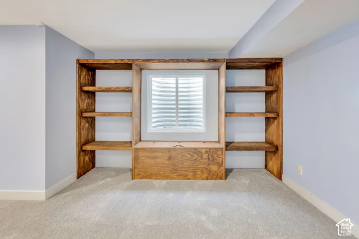 Built-in shelving with a central window, warm wood-finish cabinetry, light-toned carpeting, and a neutral wall color
