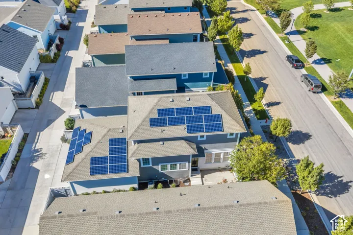 Property featuring solar panels on the roof, a light-colored exterior, and an adjacent landscaped green space with walking paths