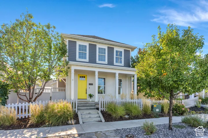 Two-story exterior with a covered porch, white picket fence, and mature landscaping