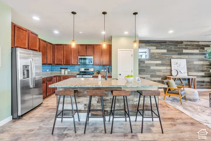Kitchen featuring wood-finish flooring, a kitchen island with pendant lighting, stone countertops, stainless steel appliances, and a tile backsplash