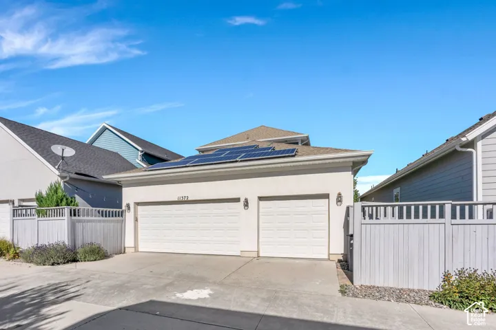 Two-car garage with white paneled doors, exterior lighting, and solar panels