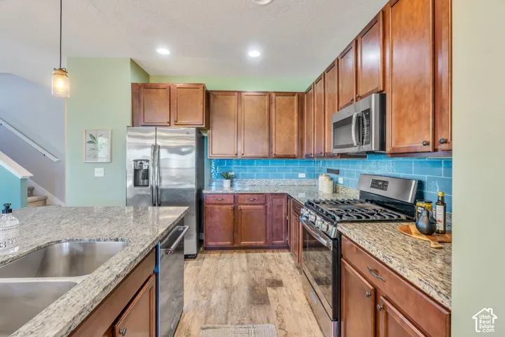 Kitchen featuring granite countertops, wood-finish flooring, stainless steel appliances, wood cabinetry, and a blue subway tile backsplash