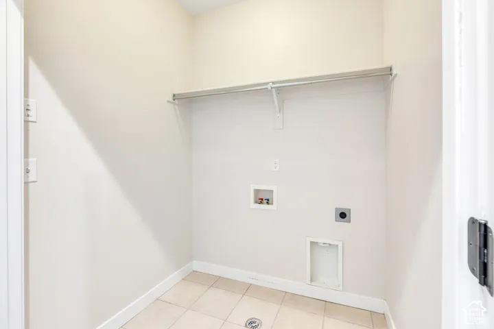 Utility space featuring a clothing rod, electrical outlets, and plumbing connections, with light-toned tile flooring