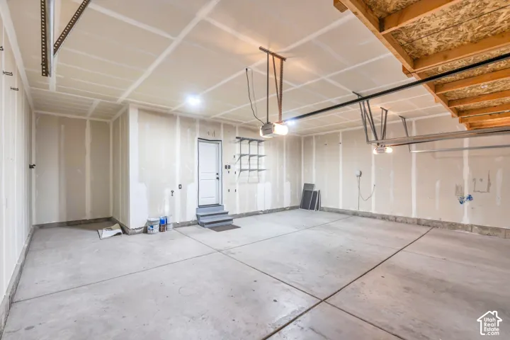 Concrete floor, exposed wood ceiling joists, overhead garage door rails, interior access door with steps, and built-in shelving
