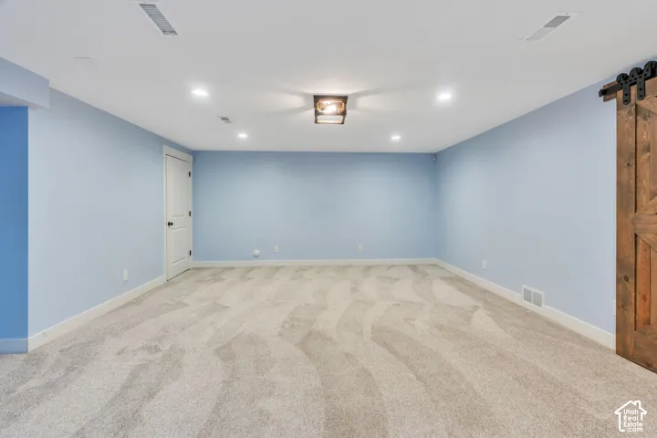 Recessed lighting, wood-finish barn door, light-toned carpet, white interior door with black hardware, and a ceiling-mounted light fixture