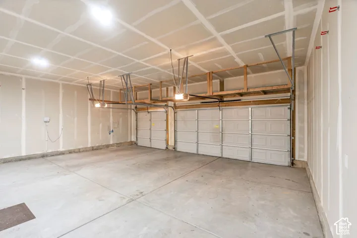 Two white panel garage doors, concrete flooring, overhead wood-frame shelving, and exposed ceiling joists