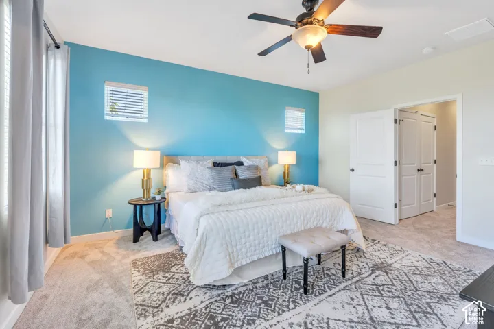Carpeted bedroom featuring a ceiling fan with light fixture, dual windows with blinds, and white bi-fold closet doors
