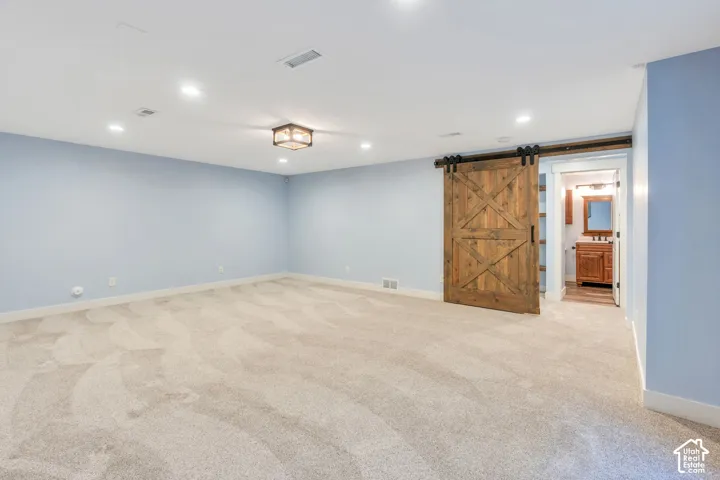 Spacious room featuring light blue walls, soft carpet flooring, recessed lighting, and a prominent wood barn door