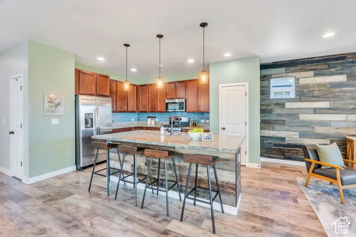 Kitchen featuring wood-finish flooring, a central island with countertop seating, stainless steel appliances, and pendant lighting