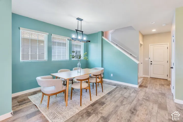 Wood-finish flooring, a contemporary linear chandelier, three windows with blinds, a white staircase with handrail, and a white entry door