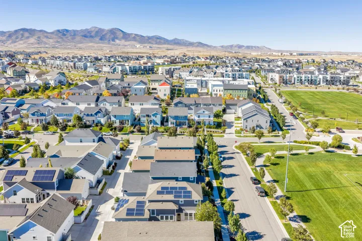 Residential neighborhood with mountain backdrop, solar panels on rooftops, paved roads, and green spaces