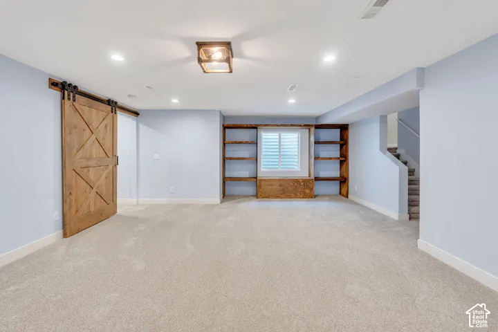 Expansive room featuring a wood-finish barn door, recessed lighting, built-in wooden shelving, and plush carpeting