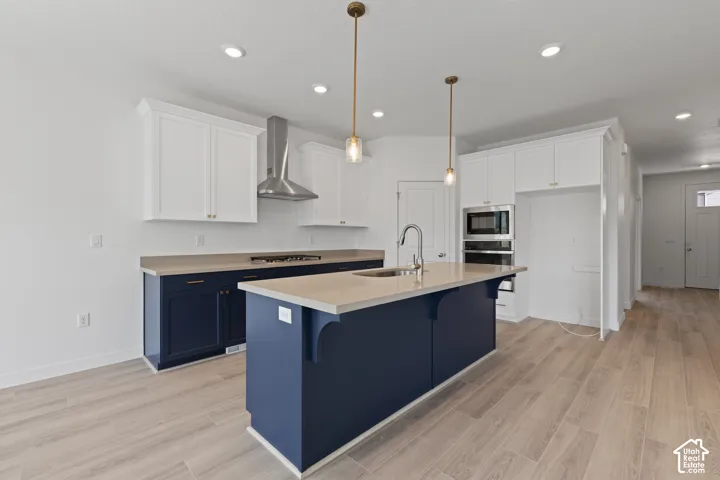 Kitchen featuring a central island with sink, two-tone cabinetry, stainless steel appliances, and pendant lighting
