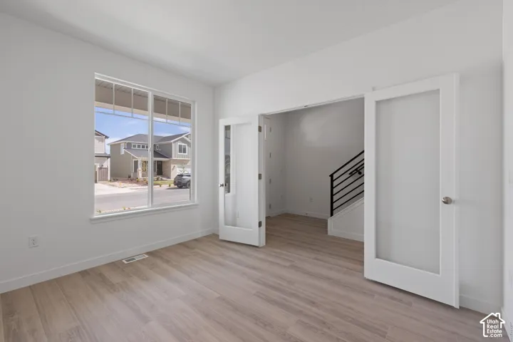 Spacious room with large windows, wood-finish flooring, and French doors featuring opaque glass panels