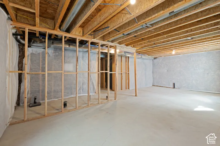 Unfinished basement featuring exposed wood joists, structural framing, concrete flooring, and foundational wall insulation
