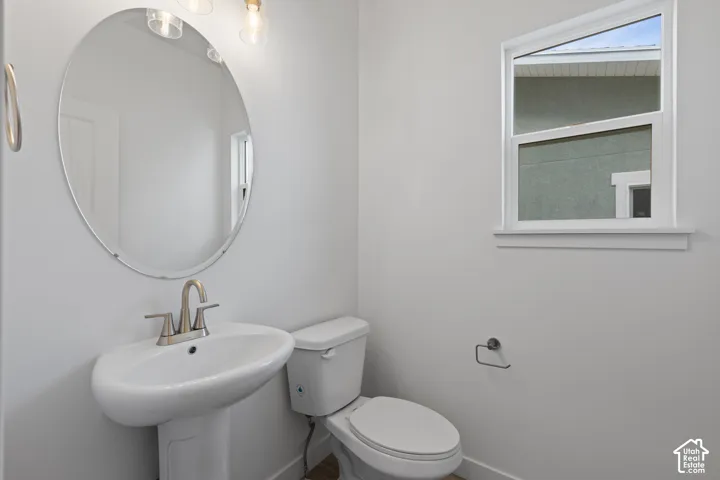 Pedestal sink with a brushed nickel faucet, large oval mirror, and a window with white trim