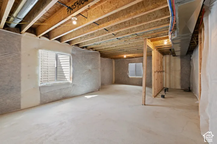 Unfinished basement featuring exposed wood joists, concrete flooring, and multiple windows