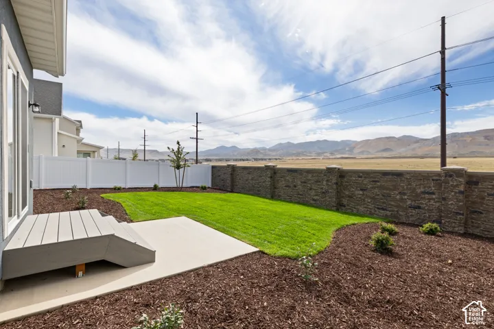 Private backyard featuring a stone-finish retaining wall, a white privacy fence, a concrete patio, and a deck with steps