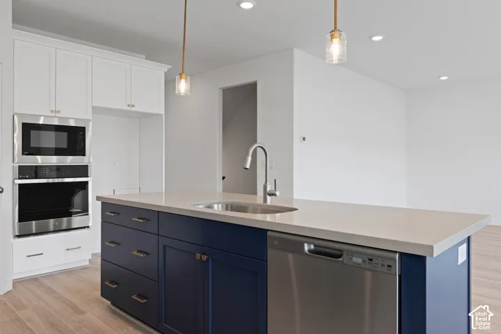 Kitchen featuring white upper cabinetry, a blue island with a built-in sink, stainless steel appliances, and wood-finish flooring