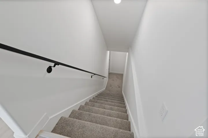 Carpeted staircase with matte black handrail and white walls
