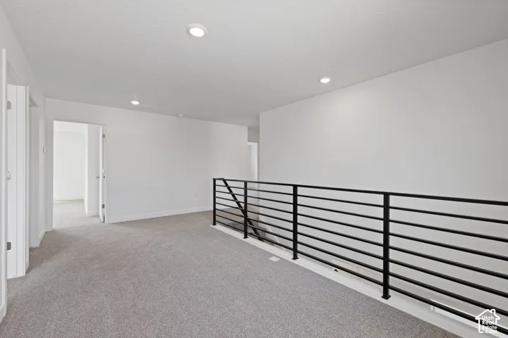 Carpeted landing area featuring a contemporary horizontal metal railing, recessed lighting, and white walls