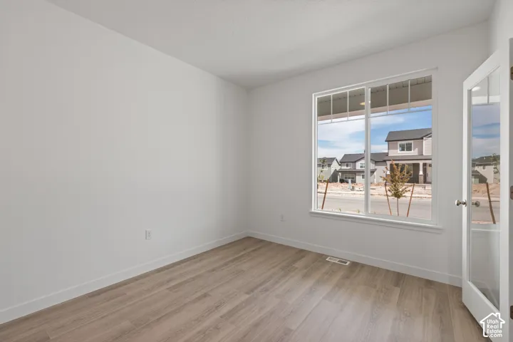 Spacious room featuring wood-finish flooring, a large window with white trim, and a glass-paneled door