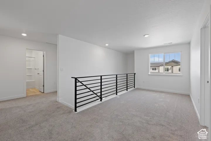 Open loft space with grey carpeting, white walls, recessed lighting, and a modern black horizontal railing