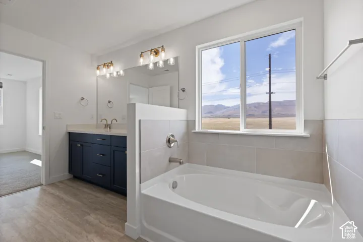 Soaking tub with tile surround, a dual vanity with a quartz countertop, and wood-finish flooring