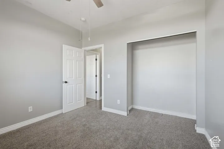 Neutral gray wall paint, light gray carpeting, open closet space, white paneled door, and a ceiling fan