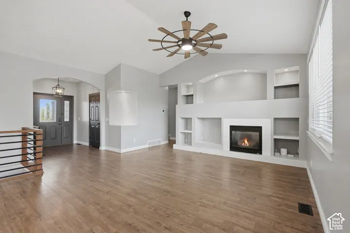 Vaulted ceiling with a ceiling fan, recessed lighting, wood-finish flooring, built-in shelving, and a gas fireplace